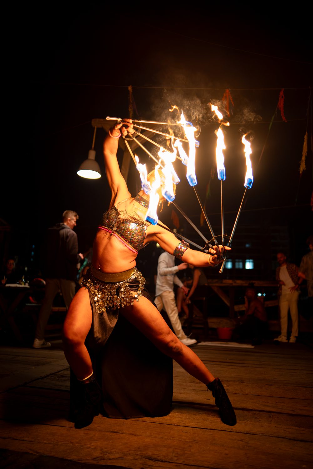Fire-fan lunge with flaming fans held wide in a sequin costume